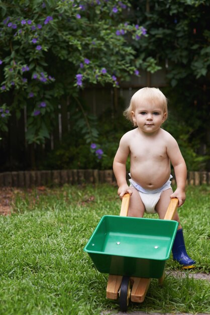 Photo portrait boy and child with a wheelbarrow garden and nature with grass playing and fun summer backyard and kid with equipment child development and countryside with plants growth and happiness