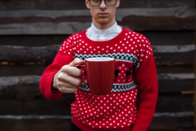 Portrait of a boy in a Christmas sweater drinking coffee, on a background of wooden wall