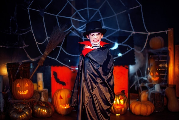 Portrait of a boy dressed in a costume of a vampire and hat over grunge background. Halloween party.