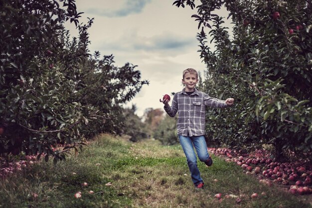 Photo portrait of boy holding apple while running on grass against sky