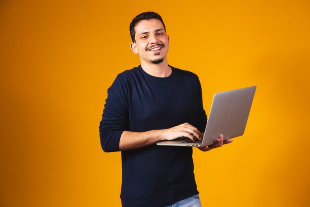 Portrait of boy holding laptop working in hands isolated over yellow background.