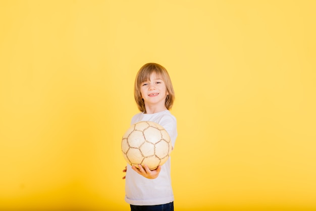 Портрет мальчика, держащего футбольный мяч, студийный желтый фон