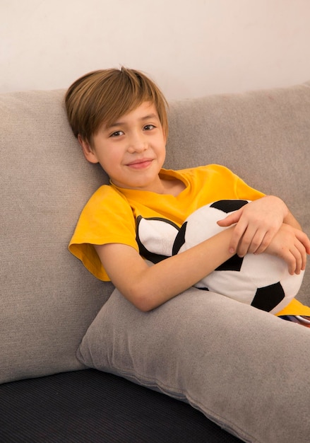 Portrait of boy holding soccer ball while sitting on sofa at home