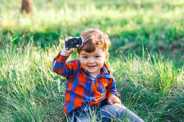 Photo portrait of boy holding toy car while sitting on field