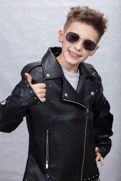 Portrait of a boy in a leather jacket and sunglasses He shows the class sign