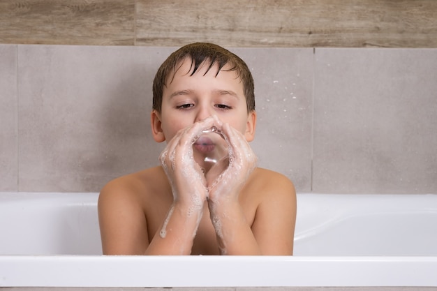 Портрет мальчика, играющего с мыльным шампунем или гелем в ванной, ребенок купается и надувает мыльные пузыри