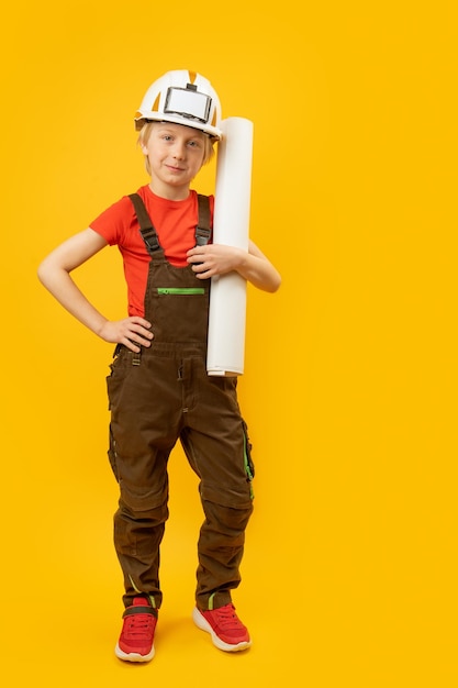 Ritratto di ragazzo in tuta da casco protettivo e con foglio di carta o disegno nelle sue mani bambino come costruttore o architetto telaio verticale