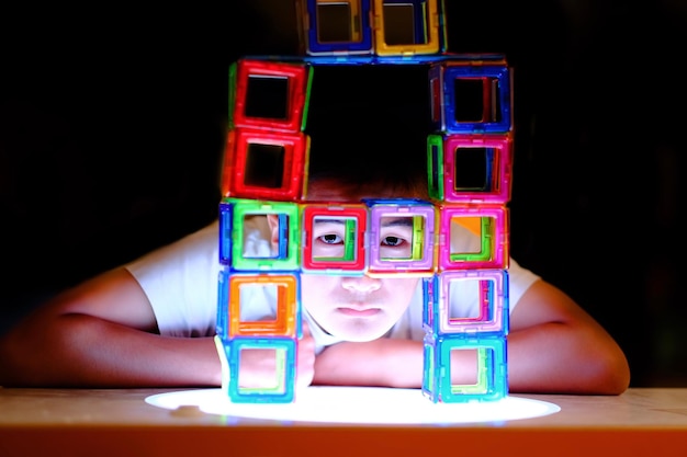 Foto ritratto di un ragazzo visto attraverso blocchi di giocattoli multicolori da un tavolo sullo sfondo nero