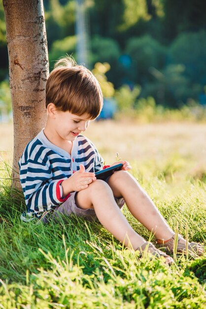 電話で草の上に座っている肖像画の少年