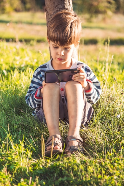 portrait boy sitting on the grass with phone