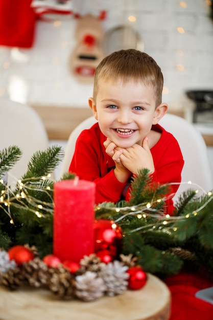 A portrait of a boy sitting in the kitchen at the Christmas table, which is decorated for the new year. Christmas decor in the kitchen