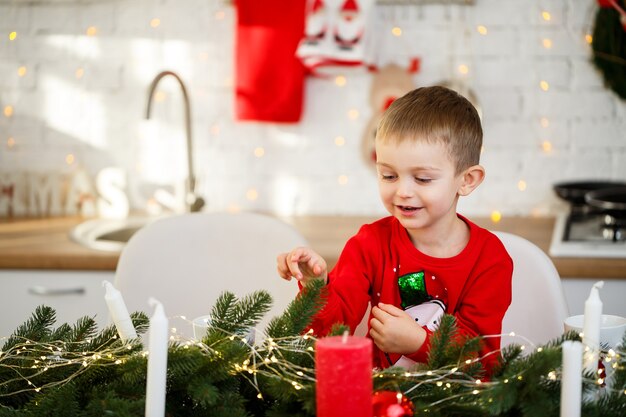 Портрет мальчика, сидящего на кухне за рождественским столом, который украшен к новому году. Новогодний декор на кухне