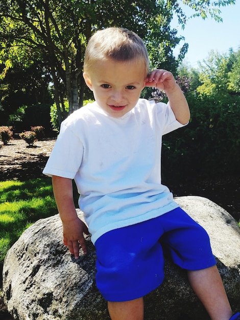 Photo portrait of boy sitting on rock at park