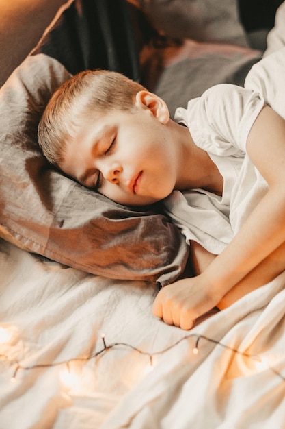 Portrait of a boy sleeping under a white blanket and with a garland christmas night baby