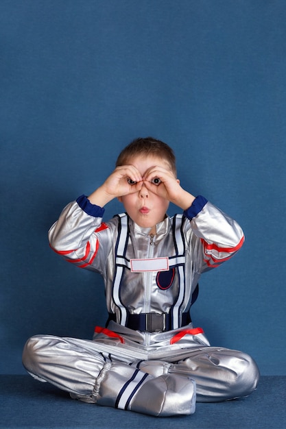 portrait of boy in space suit sitting and looking through his fingers in the form of binoculars