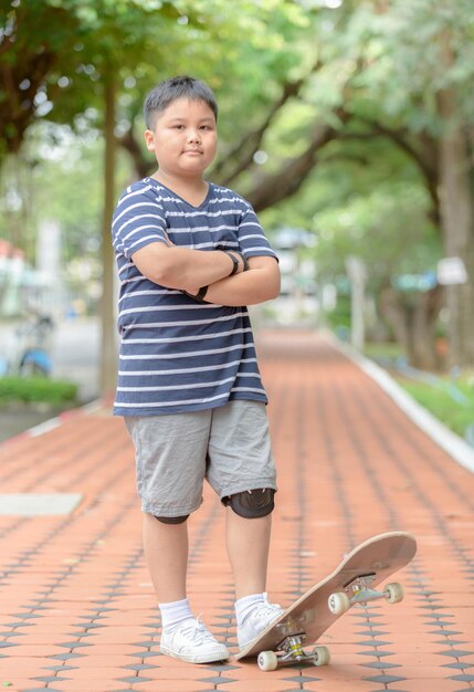 Portrait of boy standing by skateboard on footpath