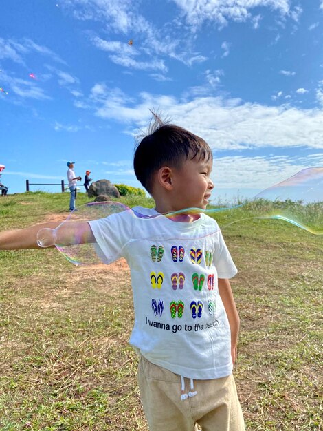 Portrait of boy standing on field against sky