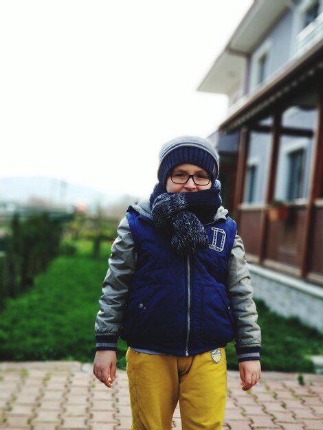 Photo portrait of boy in warm clothing standing on footpath against sky