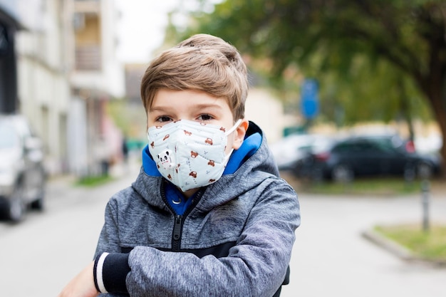 コロナウイルスパンデミックの間,屋外でマスクをかぶってカメラを見ている男の子の肖像画