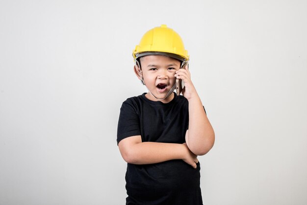 portrait of boy wearing hardhat and using phone while standing against gray background