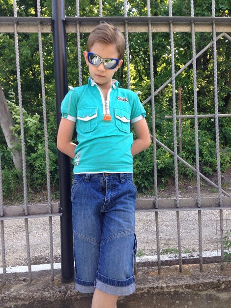 Photo portrait of boy wearing sunglasses standing against fence