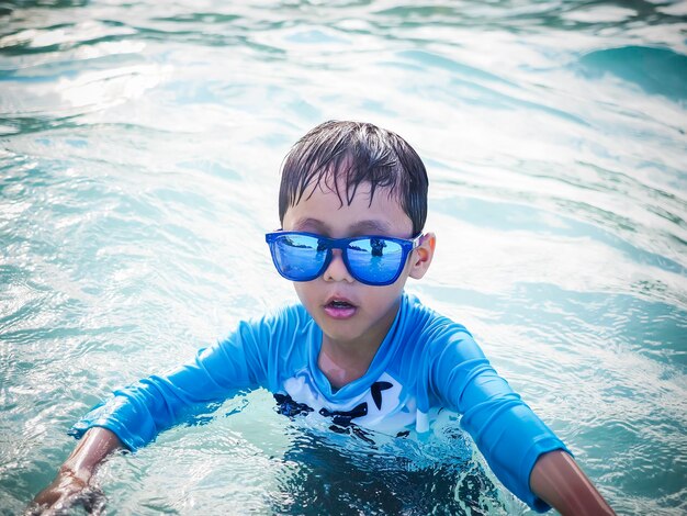 Foto ritratto di un ragazzo con gli occhiali da sole che nuota in piscina