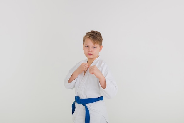 Foto ritratto di un ragazzo in un kimono bianco con una cintura blu in piedi in una posa su uno sfondo bianco