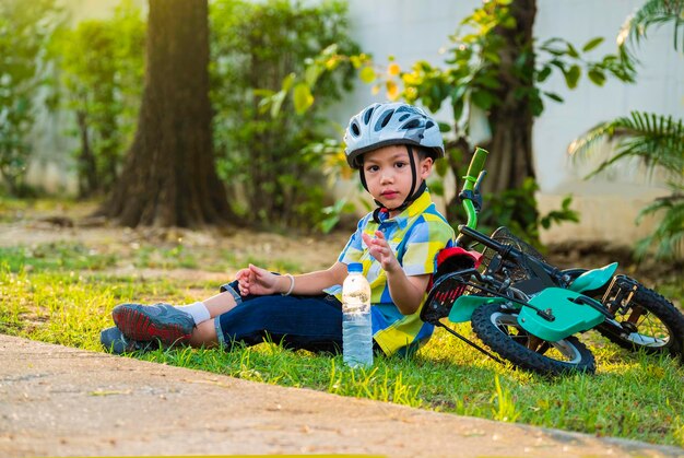 portrait of boy with bicycle sitting on grassy field in park