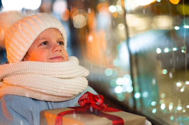 Portrait boy with gifts box looking and dreaming in christmas window shopping on traditional