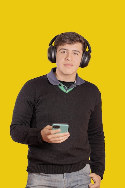 Portrait of a boy with headphones using his mobile phone isolated on yellow background