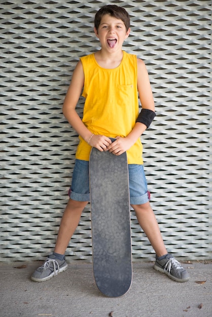 Photo portrait of boy with skateboard standing against wall