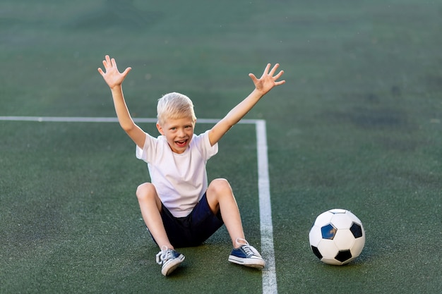 サッカーのフィールドで彼の手でサッカーボールを持つ少年のポートレート