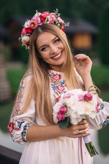 刺繡のドレスと彼女の頭に花輪を着た花嫁の肖像画。女の子は結婚式の花束を持って、カメラをのぞき込みます。