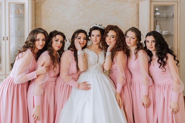 Photo portrait of the bride with her friends in the room a brunette bride in a long white dress and her friends in pink dresses are smiling and happy young girls