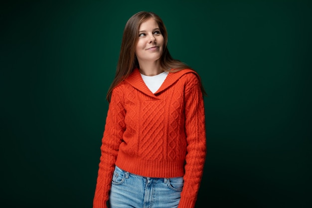 暗い緑色の背景に赤いスウェットを着た明るいポジティブな若い女性の肖像画