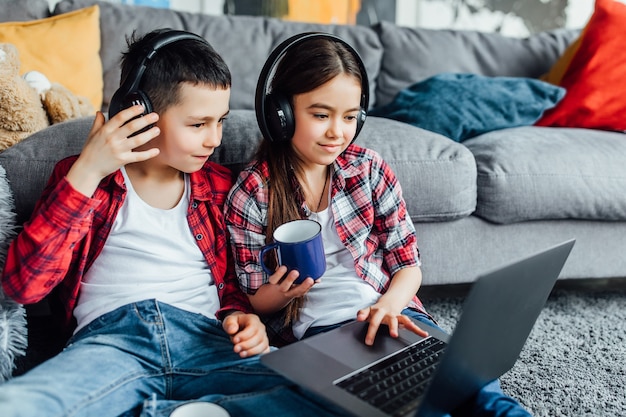 Photo portrait of brother and sister watching funny movie with headphones, while using laptop