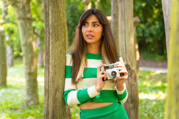 Portrait of a brunette Caucasian girl on vacation in nature taking photos with the camera wearing a green and white sweater