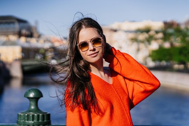 Portrait of brunette female model posing outdoors in glasses red sweater walking at street