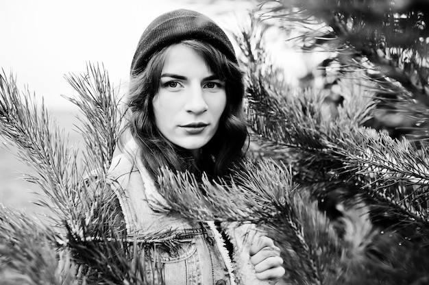 Portrait of brunette girl in hat and jeans jacket at christmas tree.