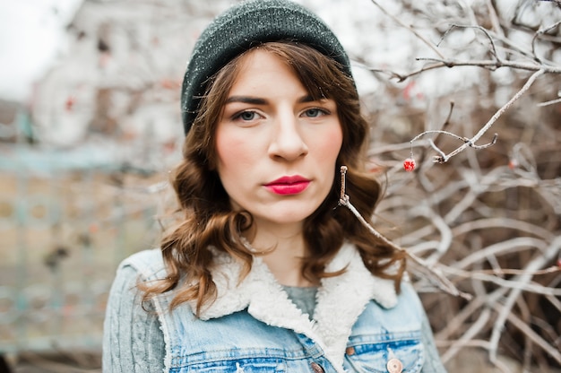 Portrait of brunette girl in hat  and jeans jacket at frozen bushes.