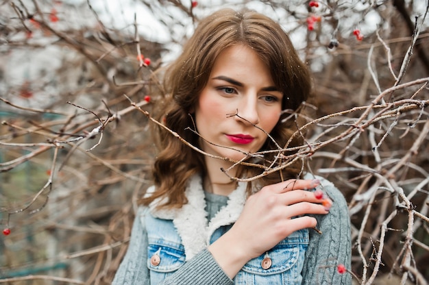 Portrait of brunette girl in jeans jacket at frozen bushes.