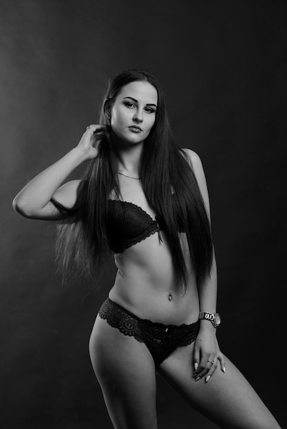 Portrait of brunette girl in underwear standing in the studio with black background.