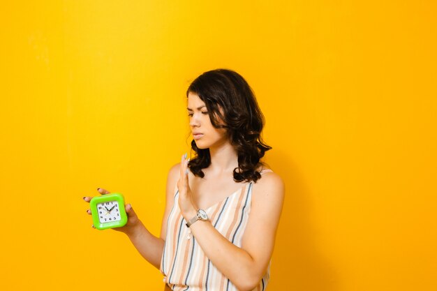 Portrait of a brunette girl who is desperate for a daily alarm on a yellow wall