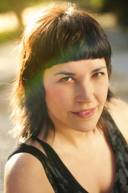 Portrait of brunette girl with bangs looking at camera with small smile on outside