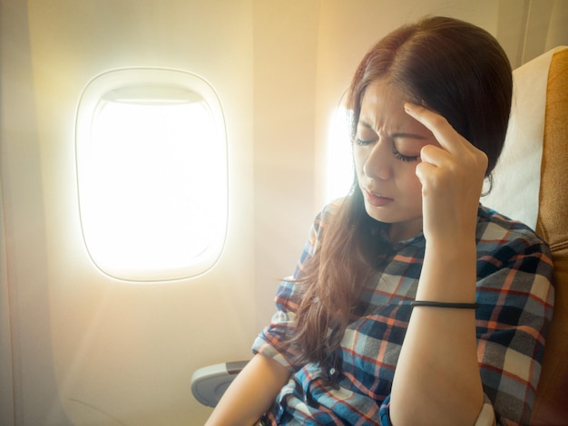 portrait of brunette hair woman headache facial expression on a chair. fear of flying student in plane with pain airsickness.