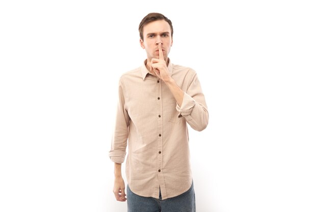 Portrait of brunette man in casual showing finger shhh isolated on white, keep silence and secret concept