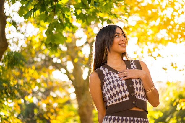 Portrait of a brunette model in autumn at sunset in a natural park smiling
