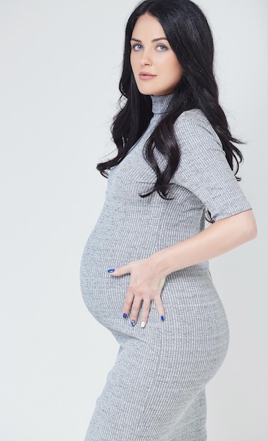 Portrait of brunette pregnant woman in a grey dress. Isolated on a grey background.