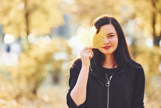 Portrait of brunette that have fun with leaves in beautiful autumn park.