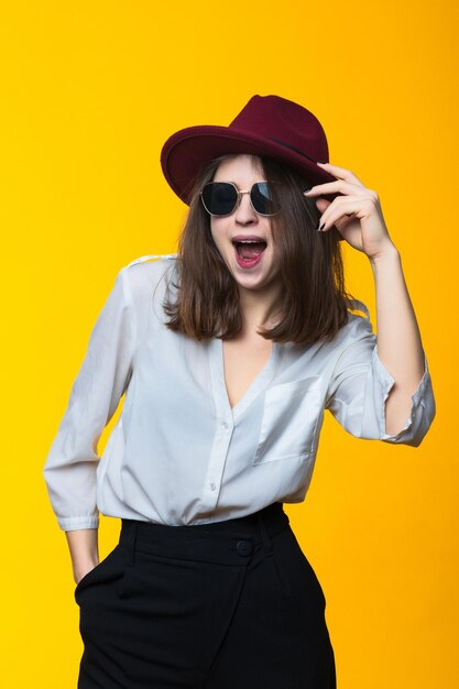 Portrait of a brunette in a white shirt hat and glasses on a yellow background